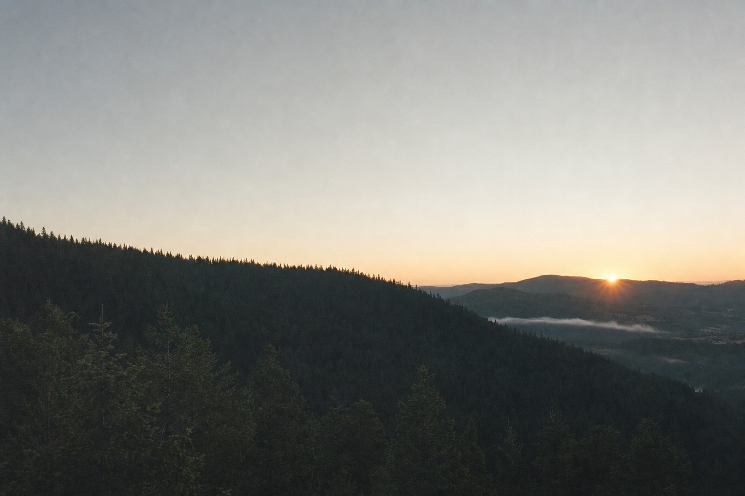First light breaking over a dark forested ridgeline